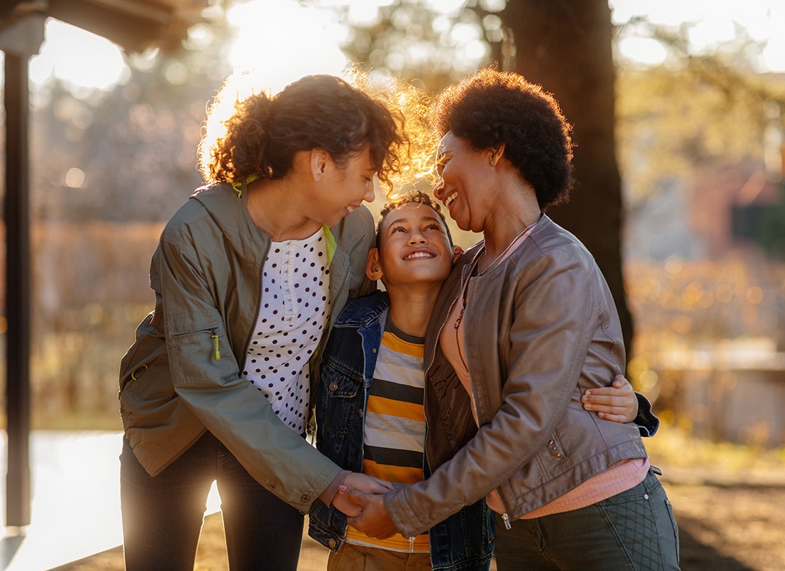 About Our Agency - Closeup Portrait of Two Moms Holding Hands and Hugging Their Young Son as They Stand Outside in the Backyard on a Sunny Fall Day.jpg