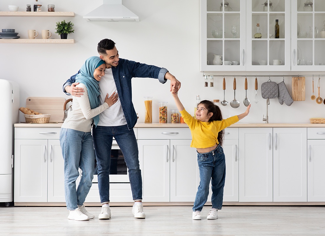 Personal Insurance - Portrait of Smiling Young Parents Having Fun Playing with Their Young Daughter as They Spin her Around in the Kitchen at Home