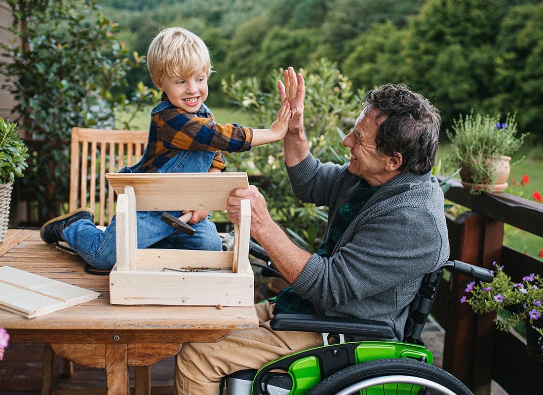 Service Center - Closeup Portrait of a Grandfather in a Wheelchair Giving his Grandson High Five as They Both Have Fun Working on a DIY Bird House Project Together